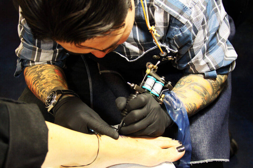 Tattooed artist in black gloves working on a client's ankle